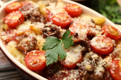 Photo of Delicious pasta casserole with cheese, tomatoes, parsley and minced meat in baking dish on table, closeup