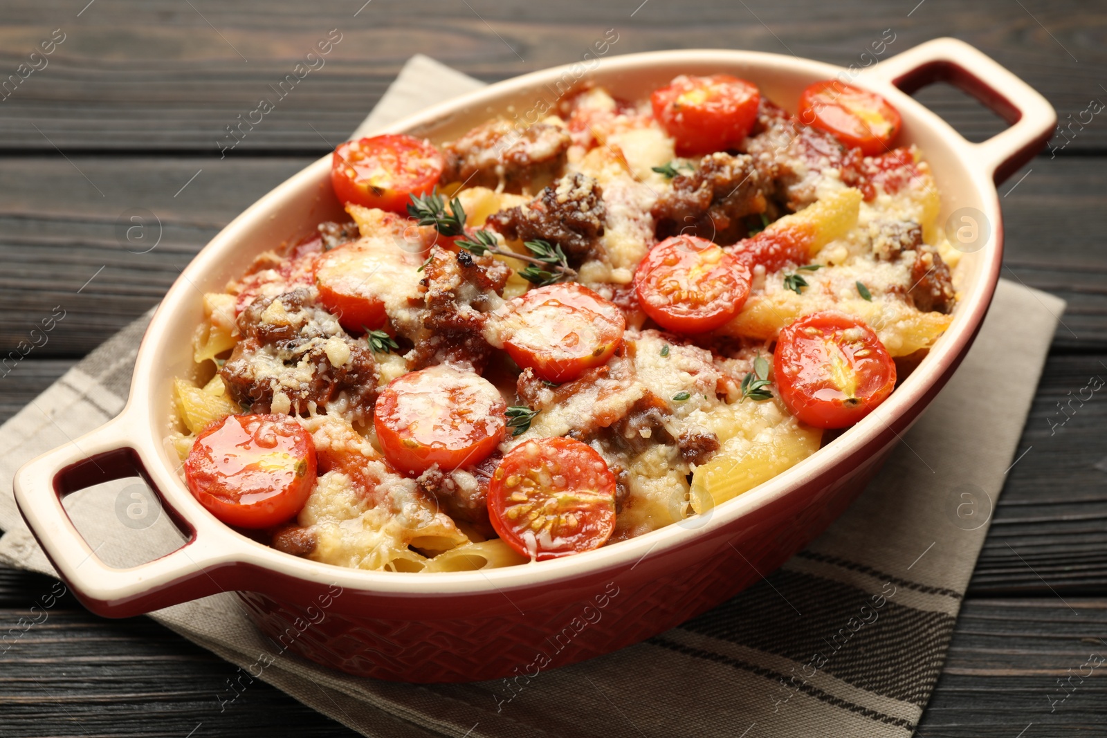 Photo of Delicious pasta casserole with cheese, tomatoes, minced meat and thyme in baking dish on wooden table, closeup