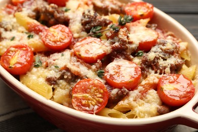 Photo of Delicious pasta casserole with cheese, tomatoes, minced meat and thyme in baking dish on table, closeup