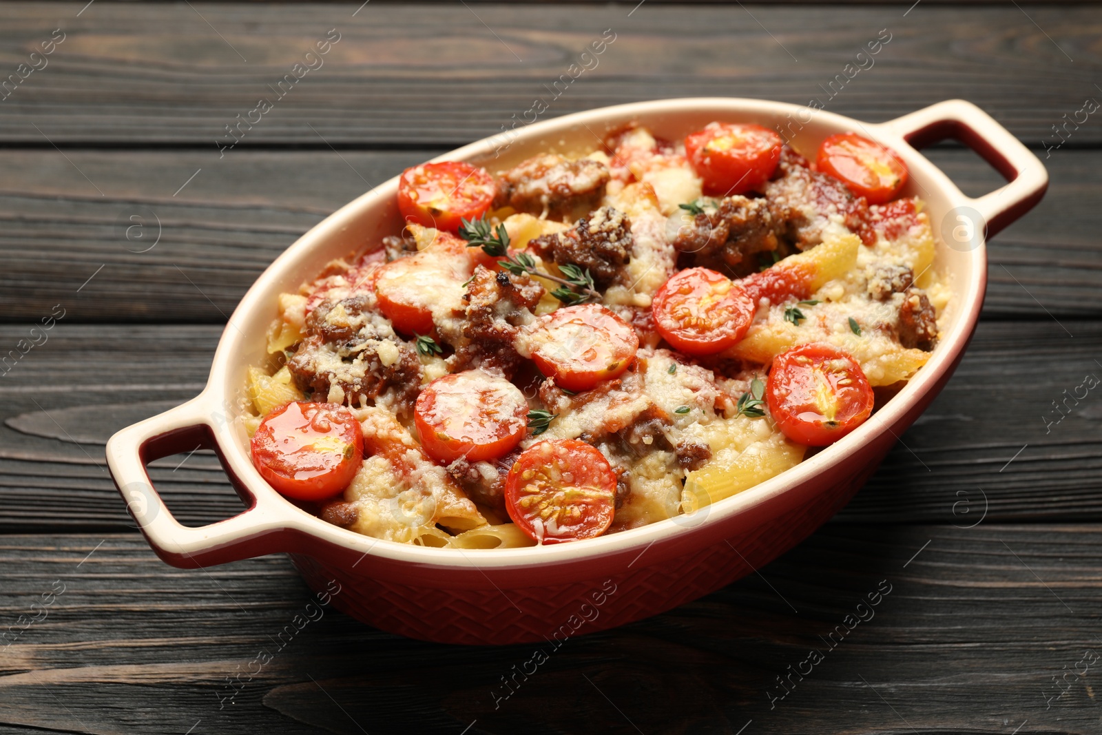 Photo of Delicious pasta casserole with cheese, tomatoes, minced meat and thyme in baking dish on wooden table, closeup