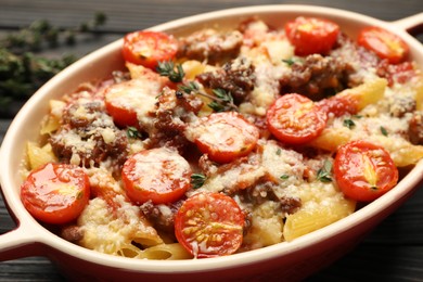 Photo of Delicious pasta casserole with cheese, tomatoes, minced meat and thyme in baking dish on table, closeup