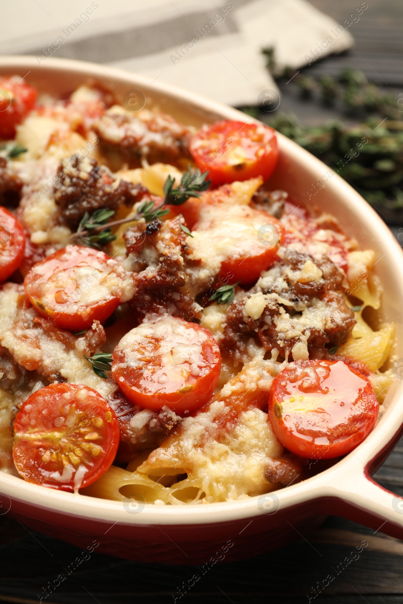 Photo of Delicious pasta casserole with cheese, tomatoes, minced meat and thyme in baking dish on table, closeup