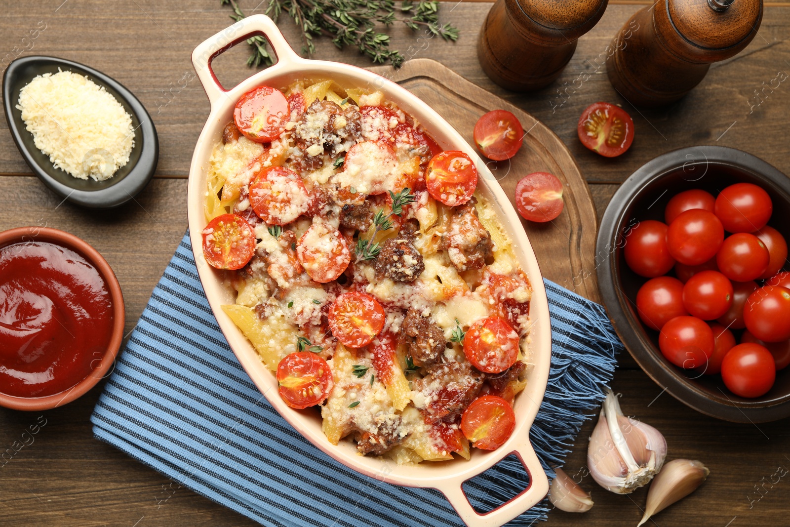 Photo of Delicious pasta casserole in baking dish with ingredients on wooden table, flat lay