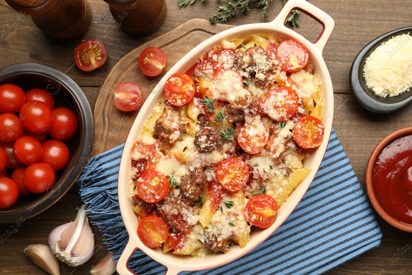 Photo of Delicious pasta casserole in baking dish with ingredients on wooden table, flat lay