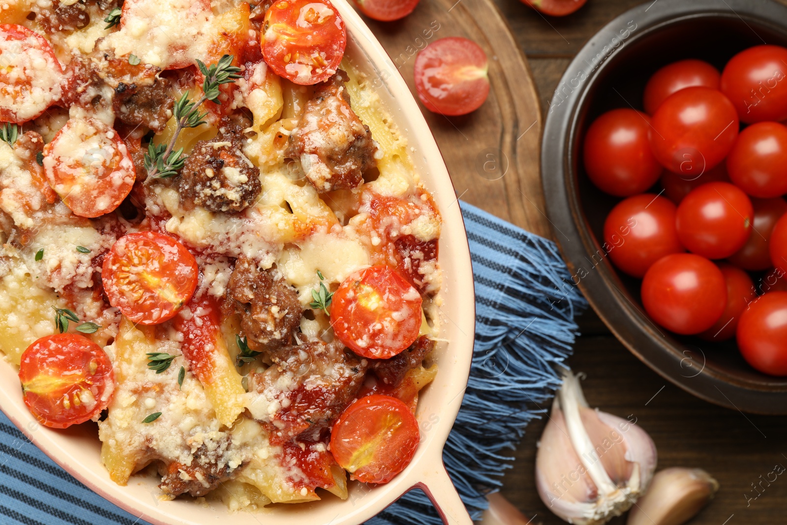 Photo of Delicious pasta casserole with cheese, tomatoes, minced meat and thyme in baking dish on wooden table, flat lay