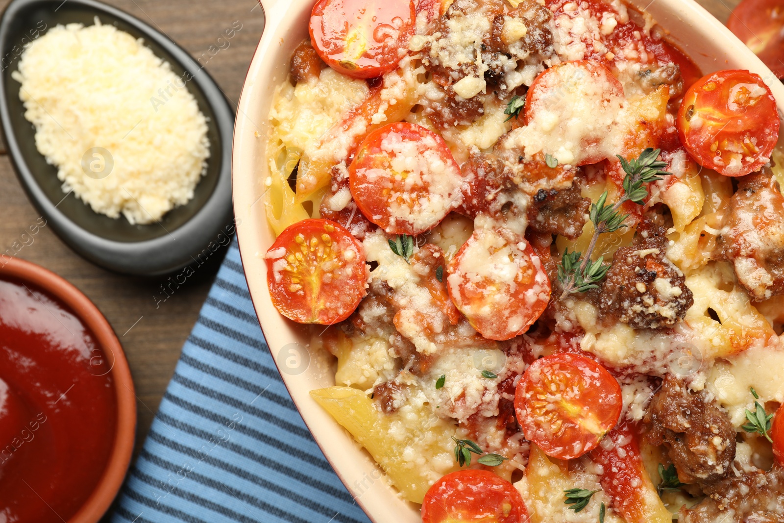 Photo of Delicious pasta casserole with cheese, tomatoes, minced meat and thyme in baking dish on wooden table, flat lay