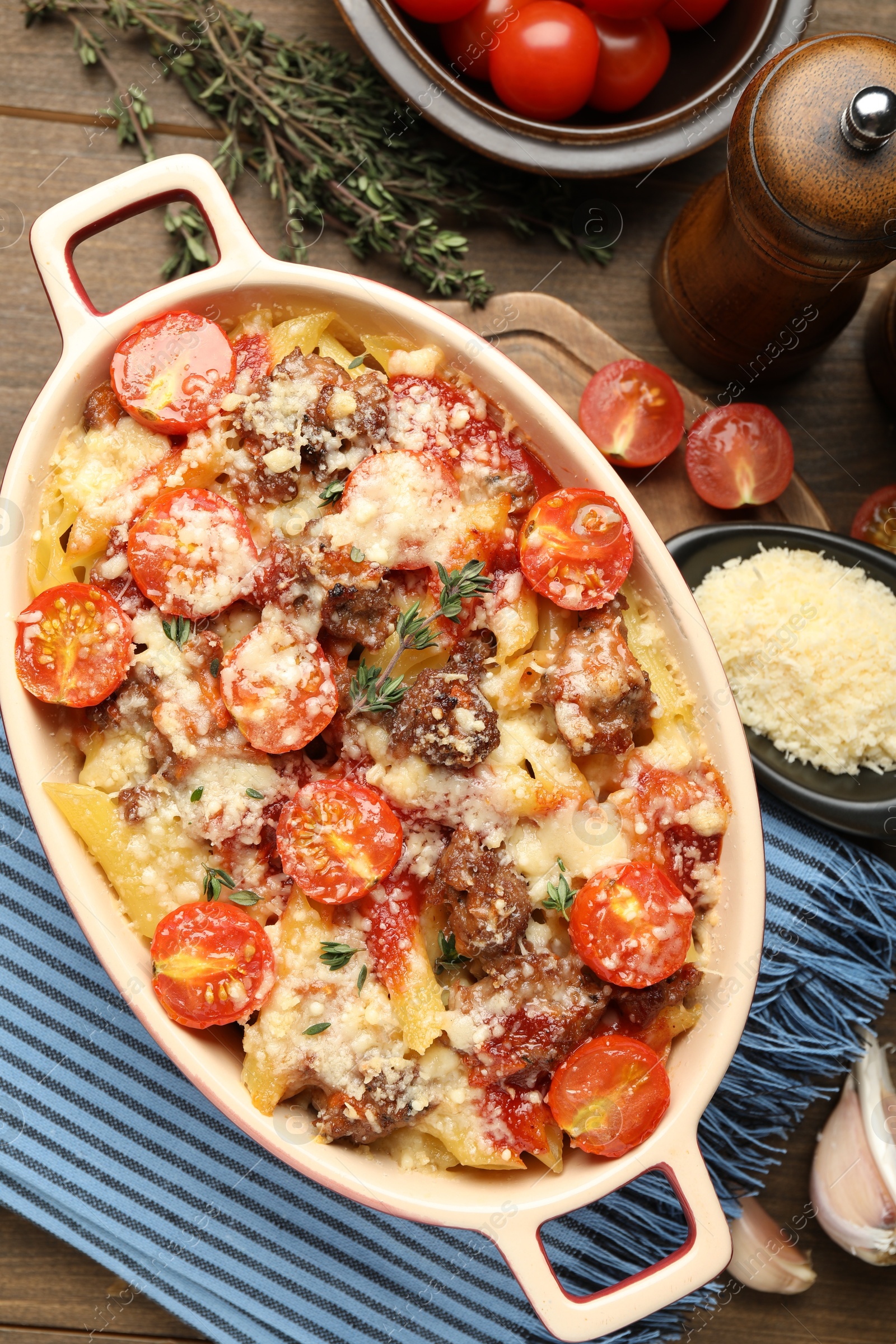 Photo of Delicious pasta casserole in baking dish with ingredients on wooden table, flat lay