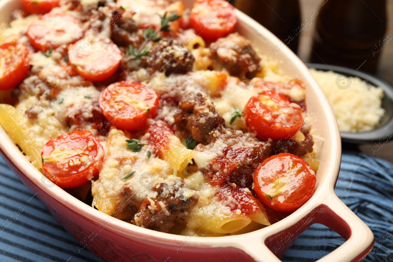 Photo of Delicious pasta casserole with cheese, tomatoes, minced meat and thyme in baking dish on table, closeup