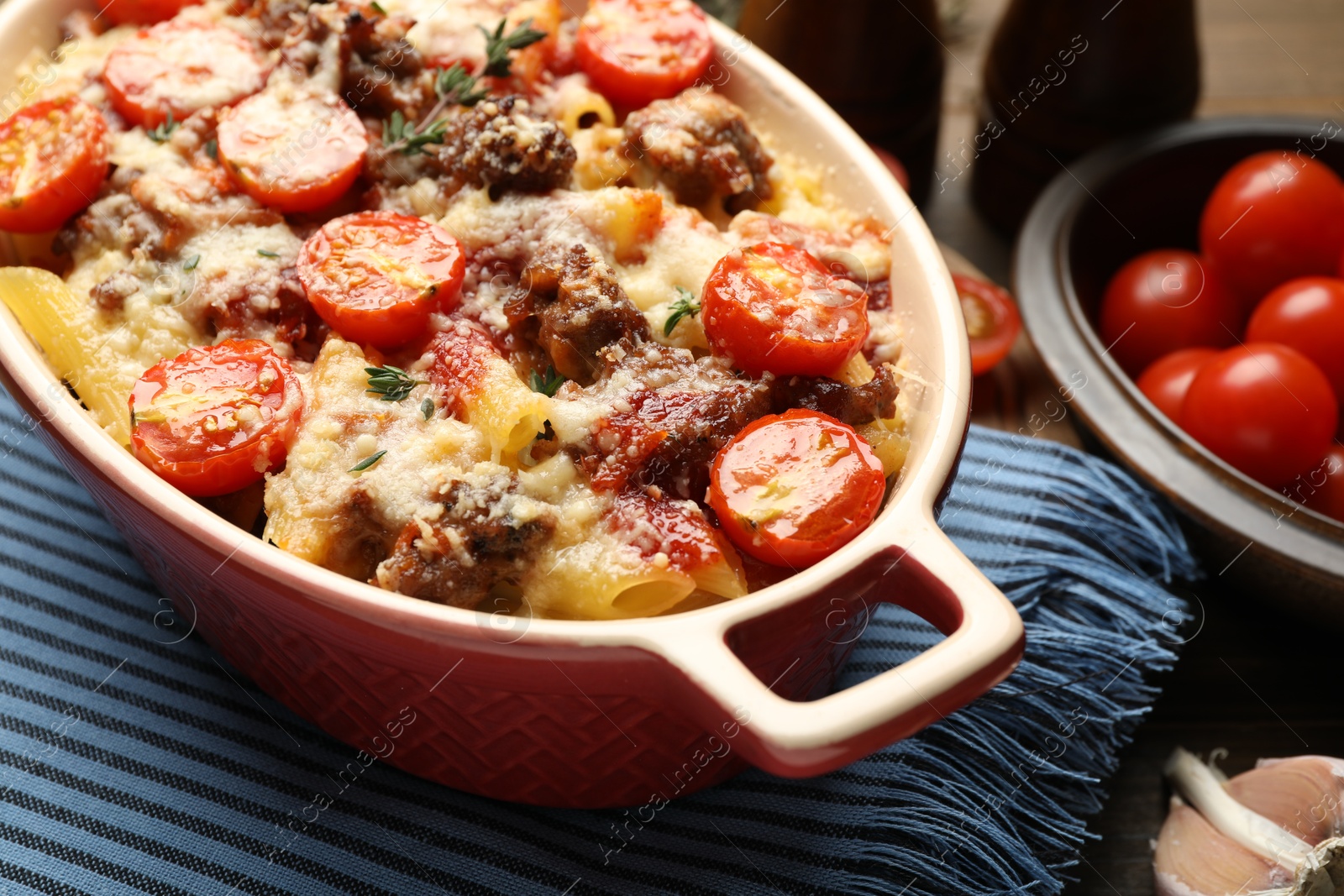 Photo of Delicious pasta casserole with cheese, tomatoes, minced meat and thyme in baking dish on table, closeup