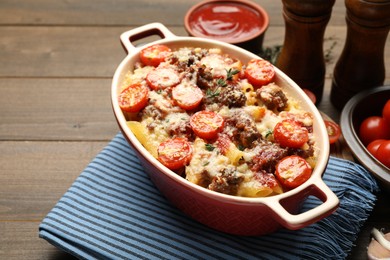 Photo of Delicious pasta casserole with cheese, tomatoes, minced meat and thyme in baking dish on wooden table, closeup