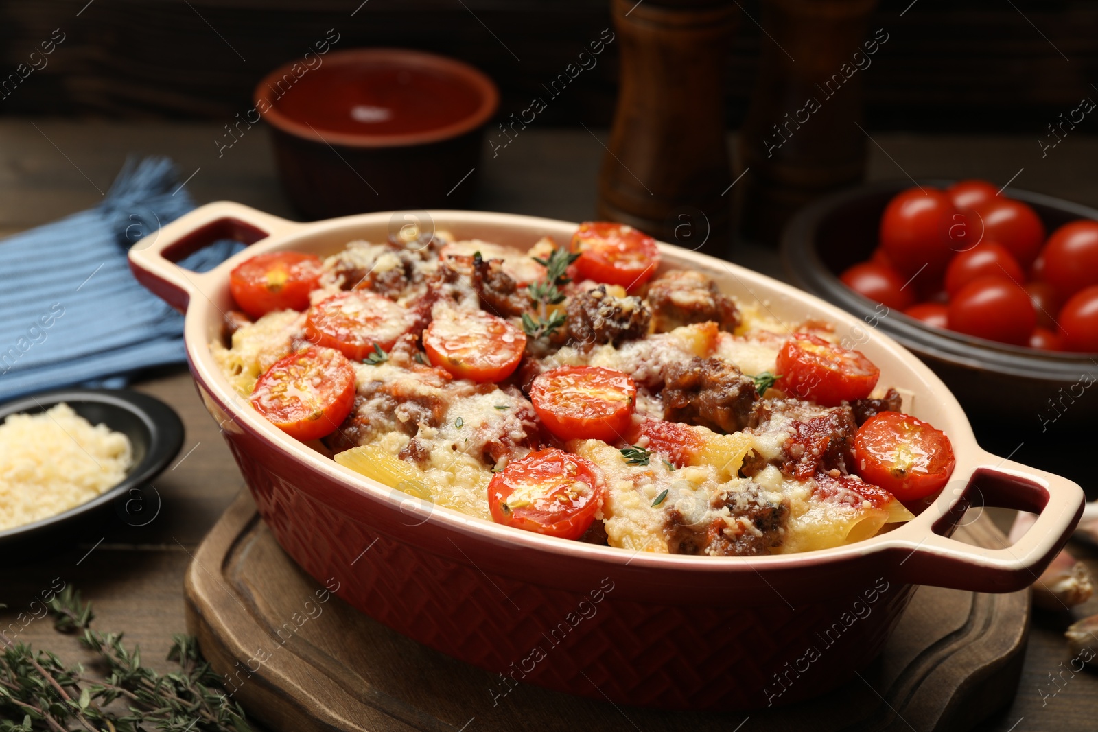 Photo of Delicious pasta casserole with cheese, tomatoes, minced meat and thyme in baking dish on wooden table, closeup