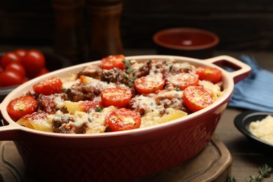 Photo of Delicious pasta casserole with cheese, tomatoes, minced meat and thyme in baking dish on table, closeup