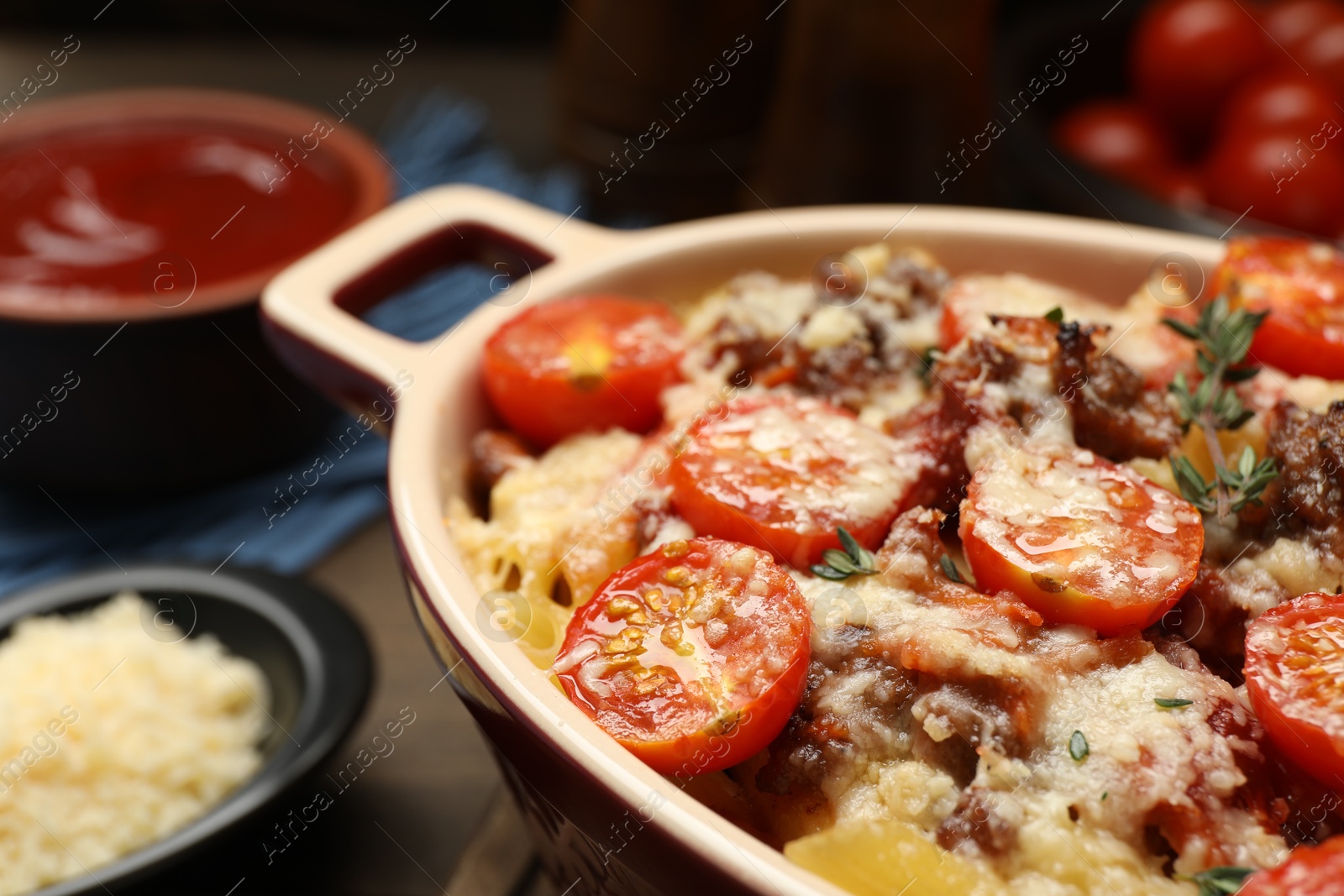 Photo of Delicious pasta casserole with cheese, tomatoes, minced meat and thyme in baking dish on table, closeup