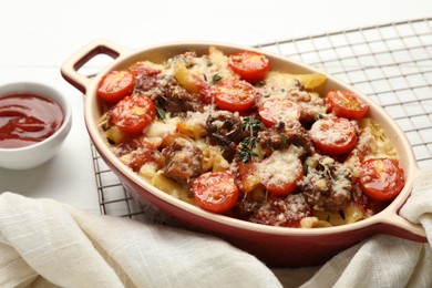 Photo of Delicious pasta casserole with cheese, tomatoes, minced meat and thyme in baking dish on white table, closeup