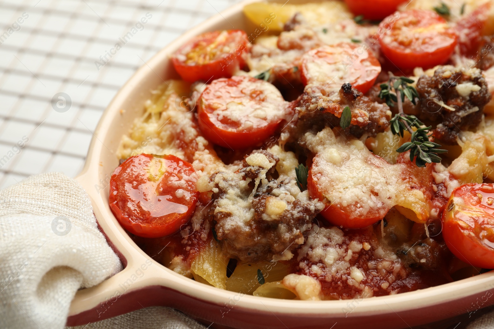 Photo of Delicious pasta casserole with cheese, tomatoes, minced meat and thyme in baking dish on white table, closeup