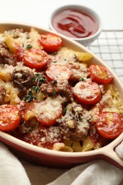 Photo of Delicious pasta casserole with cheese, tomatoes, minced meat and thyme in baking dish on white table, closeup