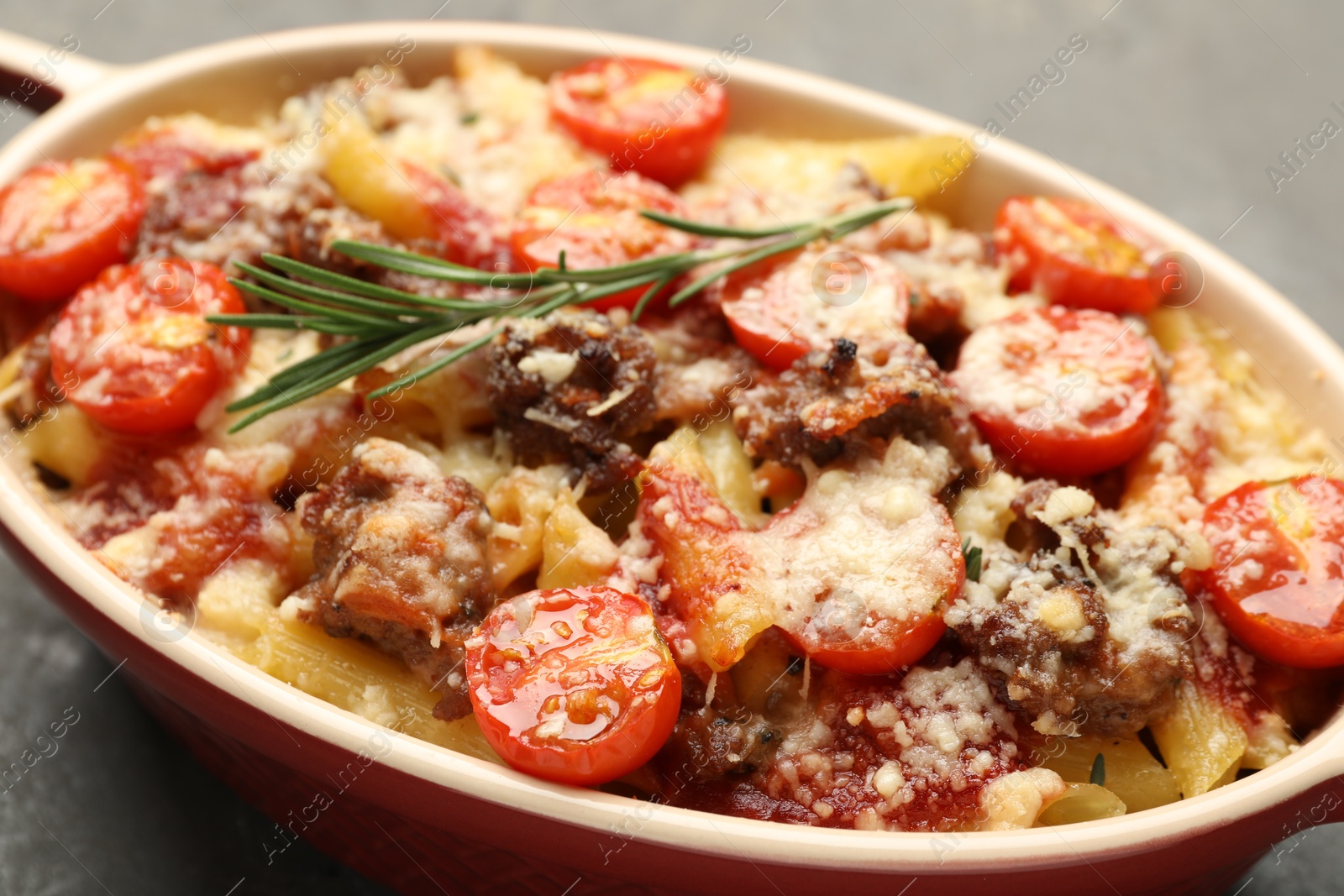 Photo of Delicious pasta casserole with cheese, tomatoes, minced meat and rosemary in baking dish on grey table, closeup