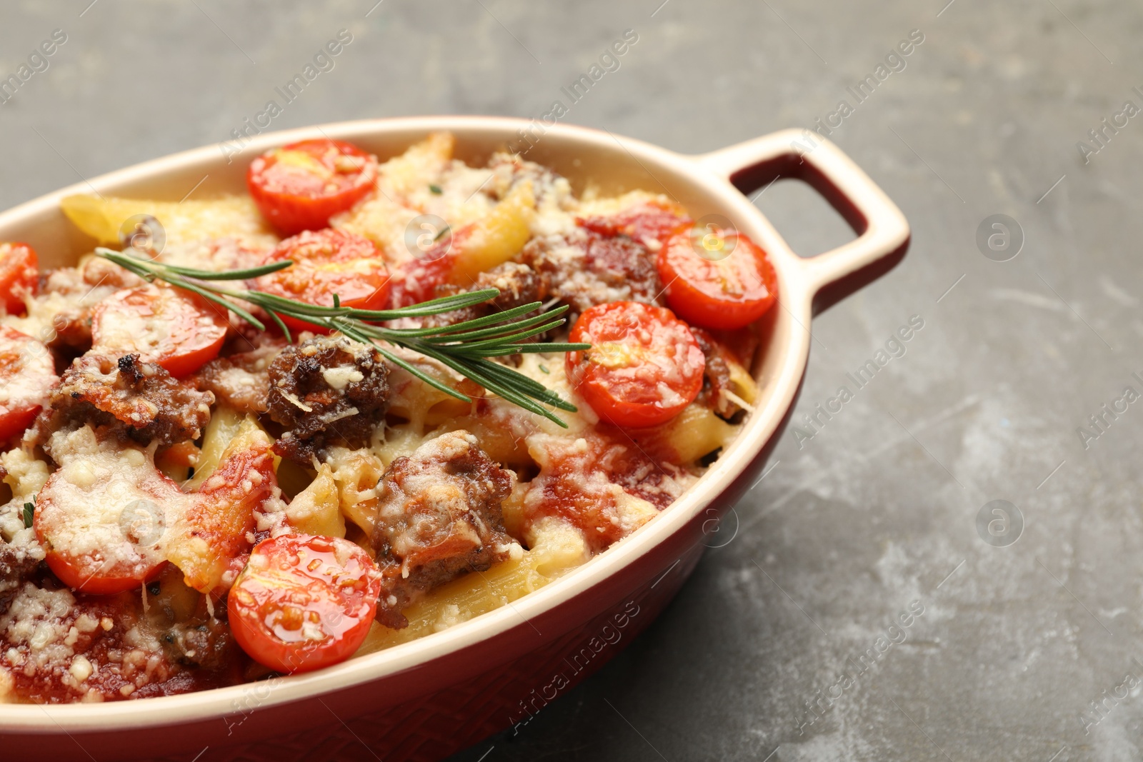 Photo of Delicious pasta casserole with cheese, tomatoes, minced meat and rosemary in baking dish on grey textured table, closeup