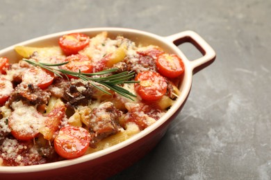 Photo of Delicious pasta casserole with cheese, tomatoes, minced meat and rosemary in baking dish on grey textured table, closeup