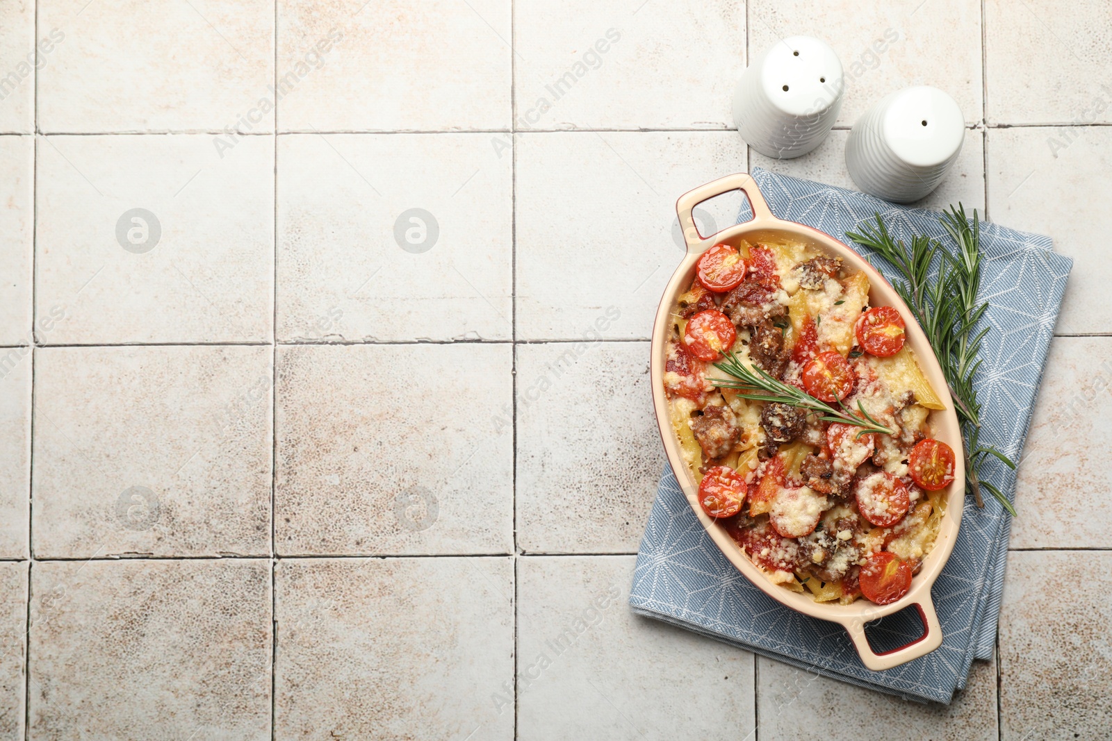 Photo of Delicious pasta casserole in baking dish, rosemary and spices on tiled table, flat lay. Space for text