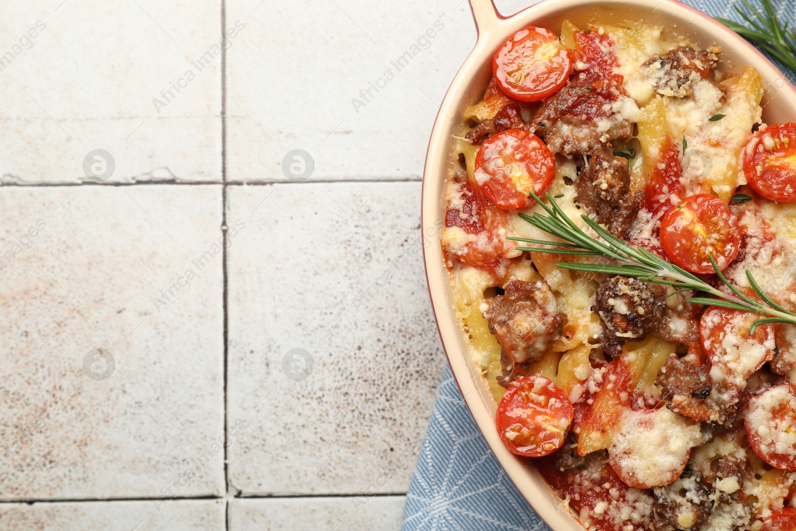 Photo of Delicious pasta casserole with cheese, tomatoes, minced meat and rosemary in baking dish on tiled table, top view. Space for text