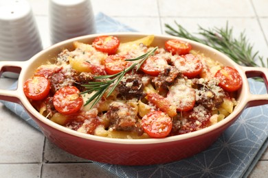 Photo of Delicious pasta casserole with cheese, tomatoes, minced meat and rosemary in baking dish on tiled table, closeup