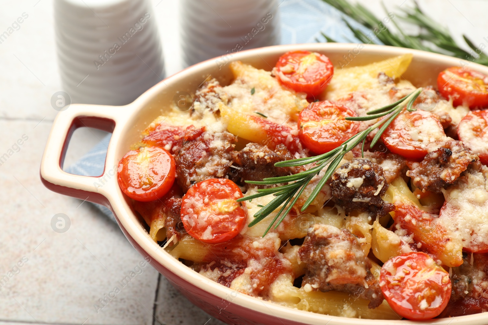 Photo of Delicious pasta casserole with cheese, tomatoes, minced meat and rosemary in baking dish on tiled table, closeup