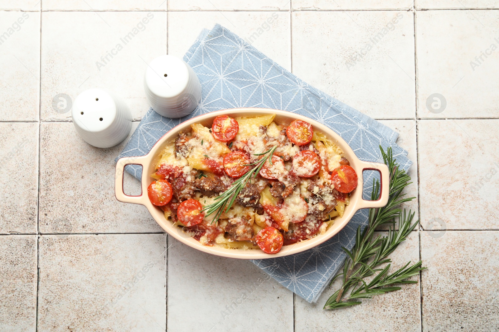 Photo of Delicious pasta casserole in baking dish, rosemary and spices on tiled table, flat lay