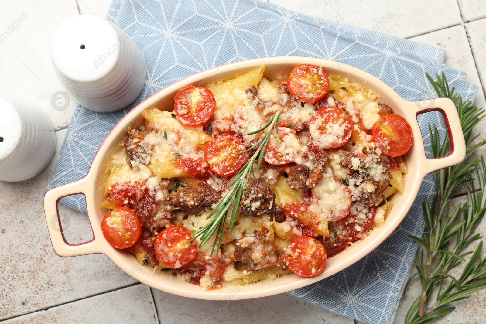 Photo of Delicious pasta casserole in baking dish, rosemary and spices on tiled table, flat lay