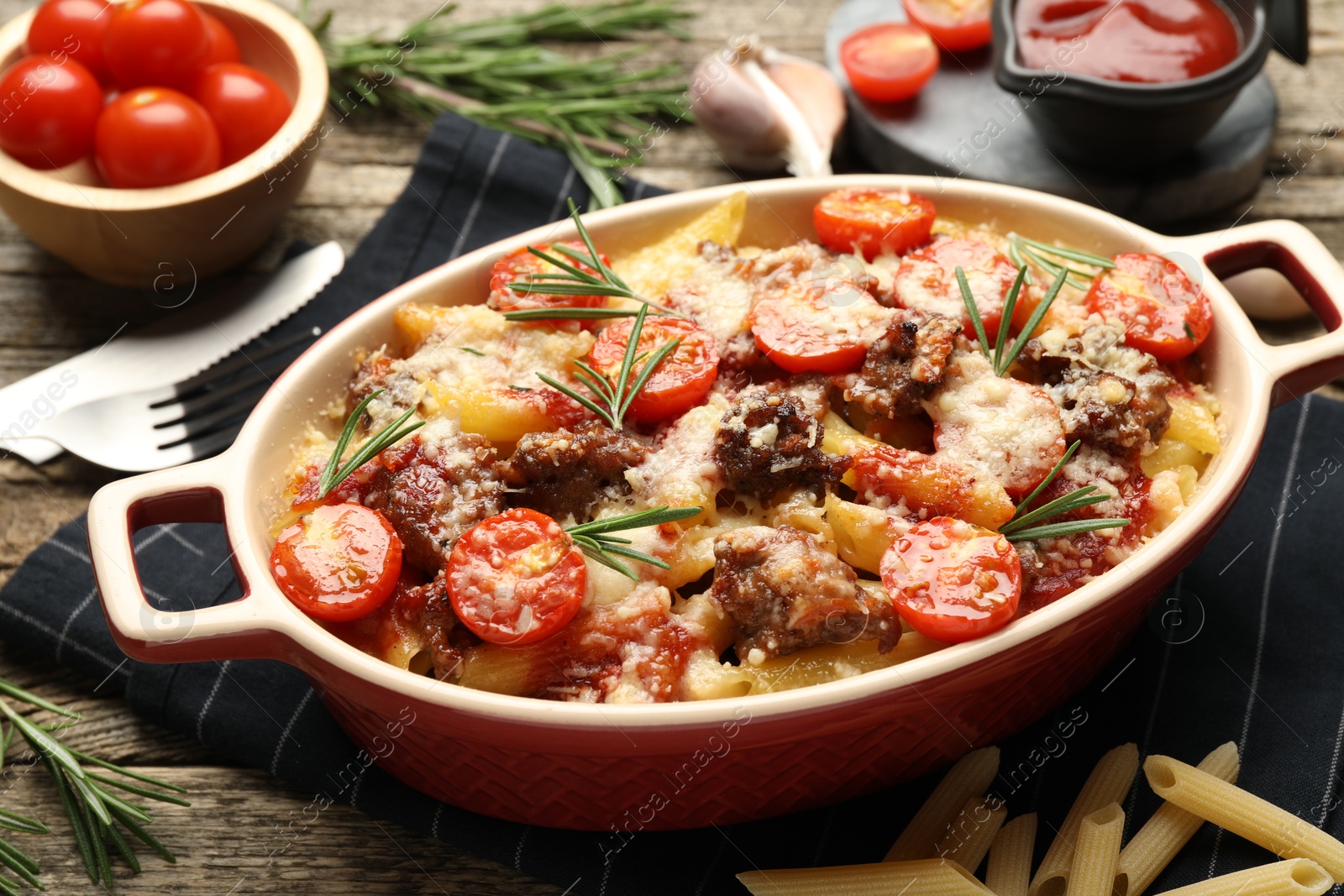 Photo of Delicious pasta casserole with cheese, tomatoes, minced meat and rosemary in baking dish on wooden table, closeup