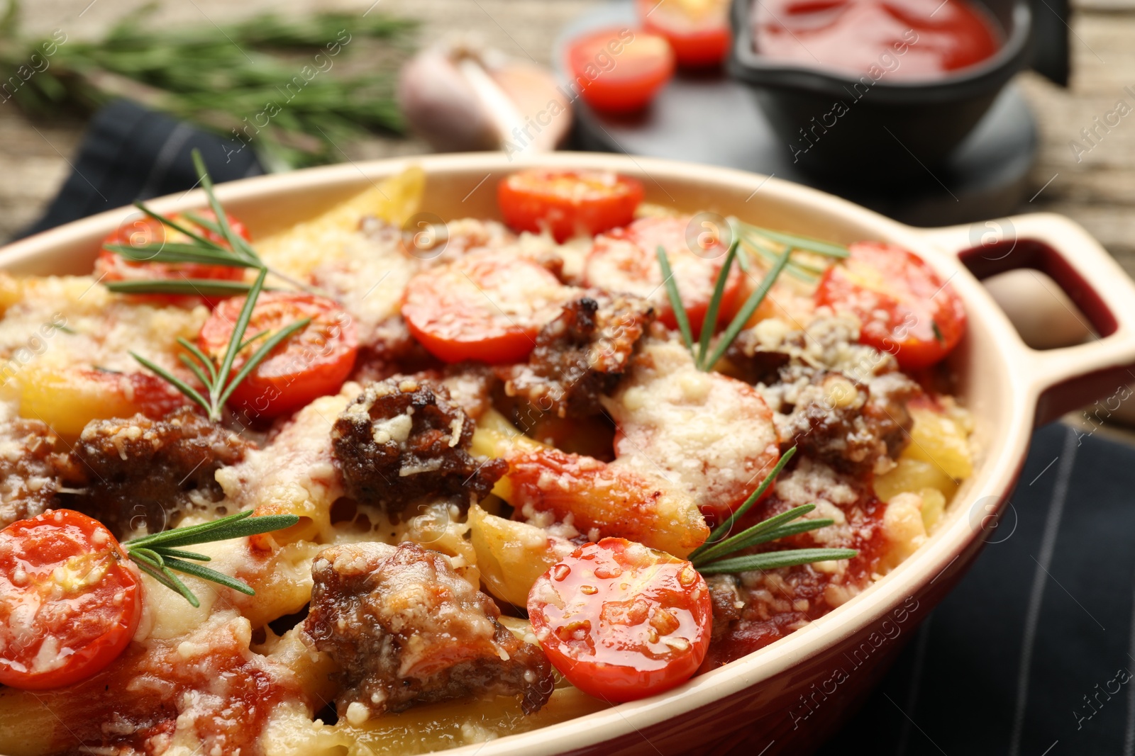 Photo of Delicious pasta casserole with cheese, tomatoes, minced meat and rosemary in baking dish on table, closeup