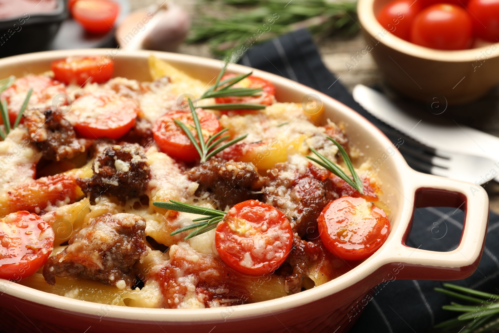 Photo of Delicious pasta casserole with cheese, tomatoes, minced meat and rosemary in baking dish on table, closeup