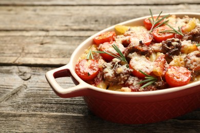 Photo of Delicious pasta casserole with cheese, tomatoes, minced meat and rosemary in baking dish on wooden table, closeup