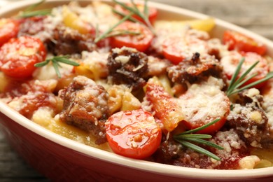 Photo of Delicious pasta casserole with cheese, tomatoes, minced meat and rosemary in baking dish on table, closeup