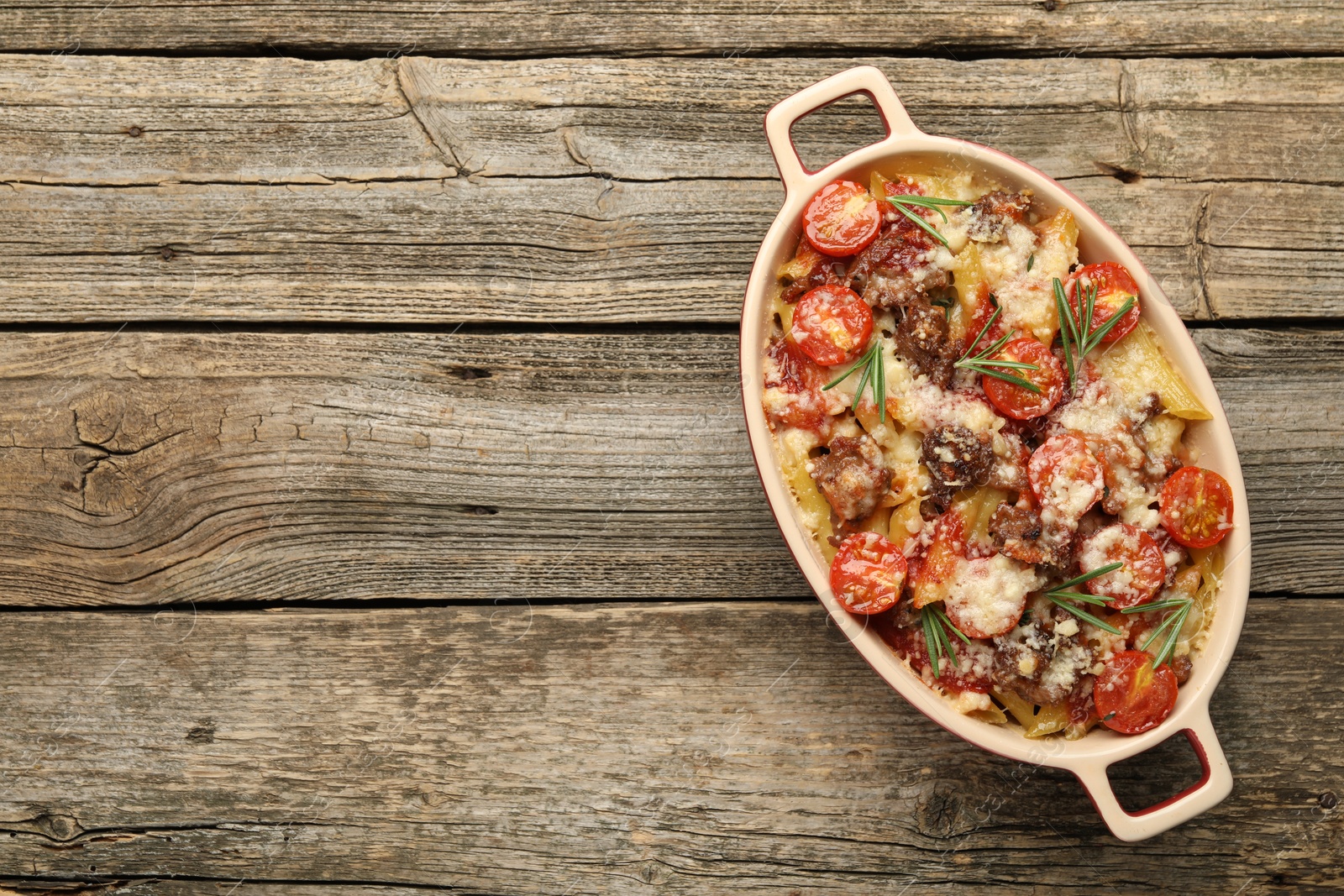 Photo of Delicious pasta casserole with cheese, tomatoes, minced meat and rosemary in baking dish on wooden table, top view. Space for text