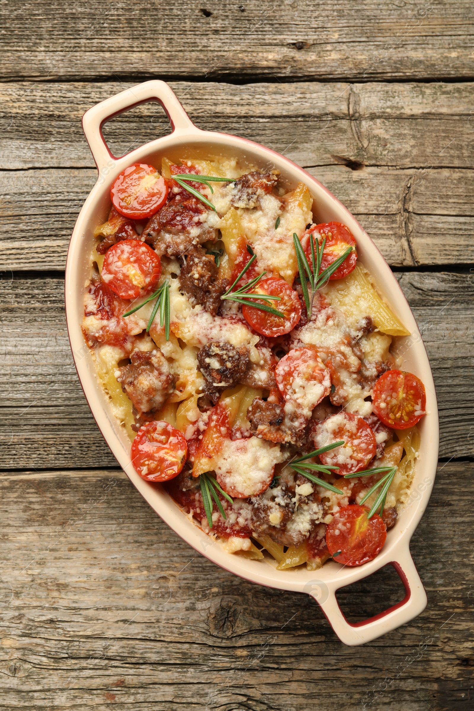 Photo of Delicious pasta casserole with cheese, tomatoes, minced meat and rosemary in baking dish on wooden table, top view