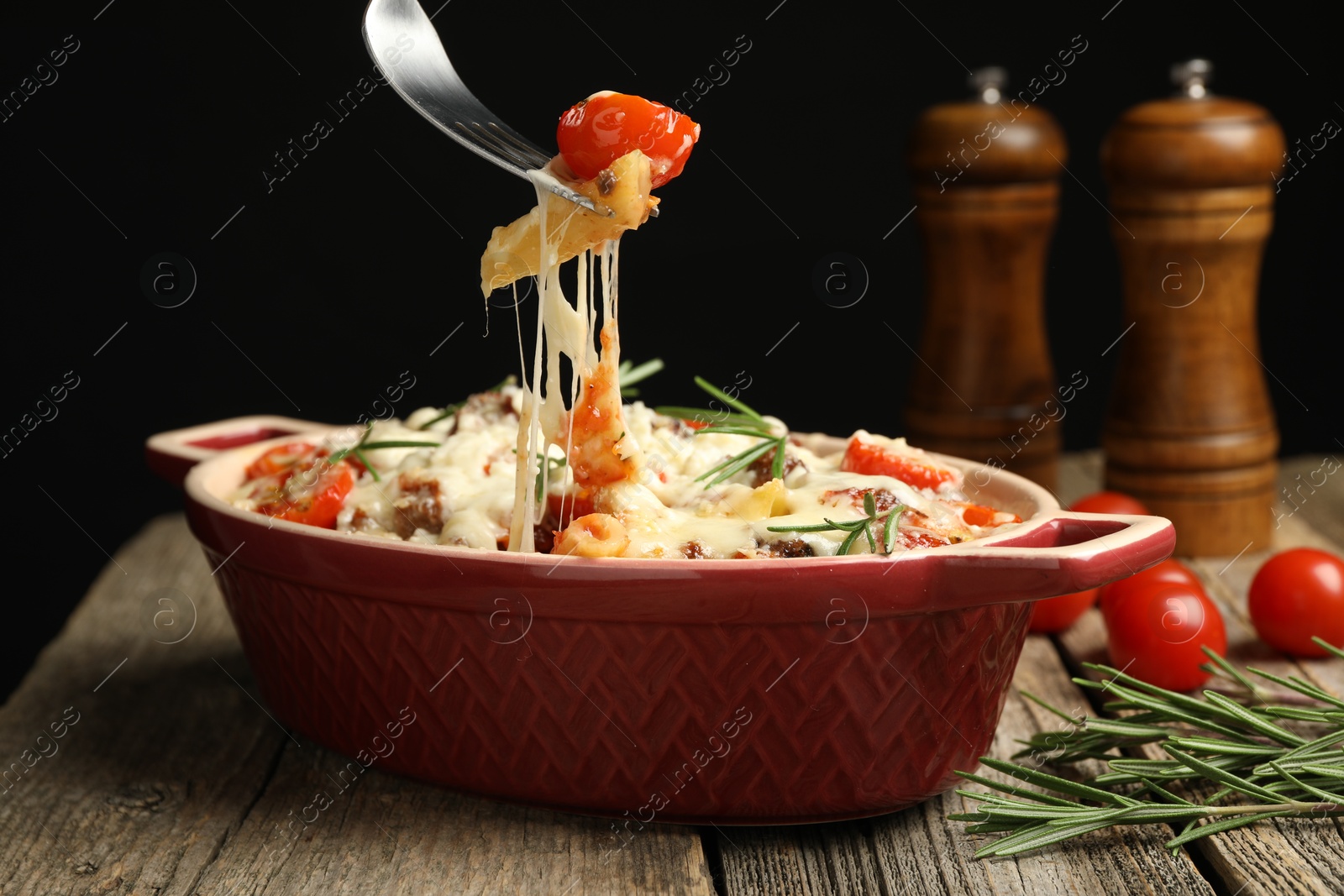 Photo of Eating delicious pasta casserole with fork at wooden table against black background, closeup