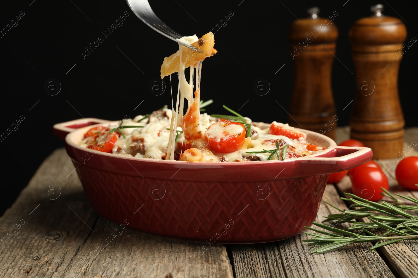 Photo of Eating delicious pasta casserole with fork at wooden table against black background, closeup