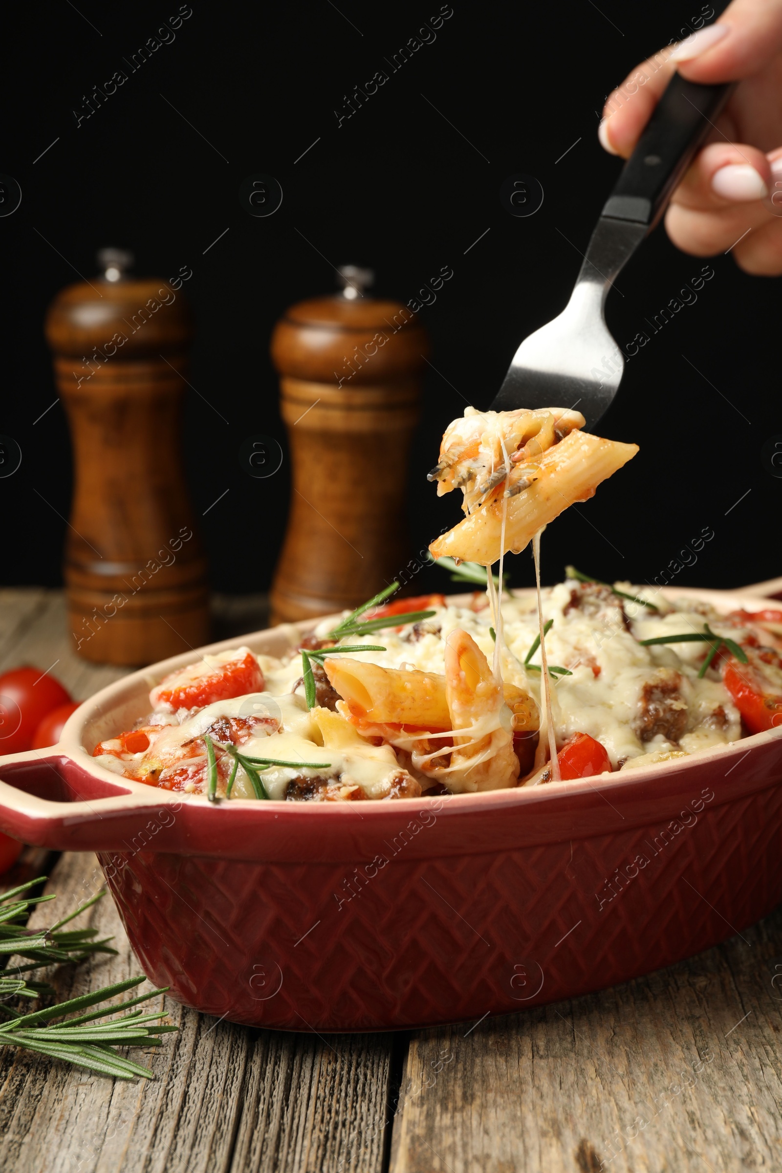 Photo of Woman eating delicious pasta casserole with fork at wooden table against black background, closeup