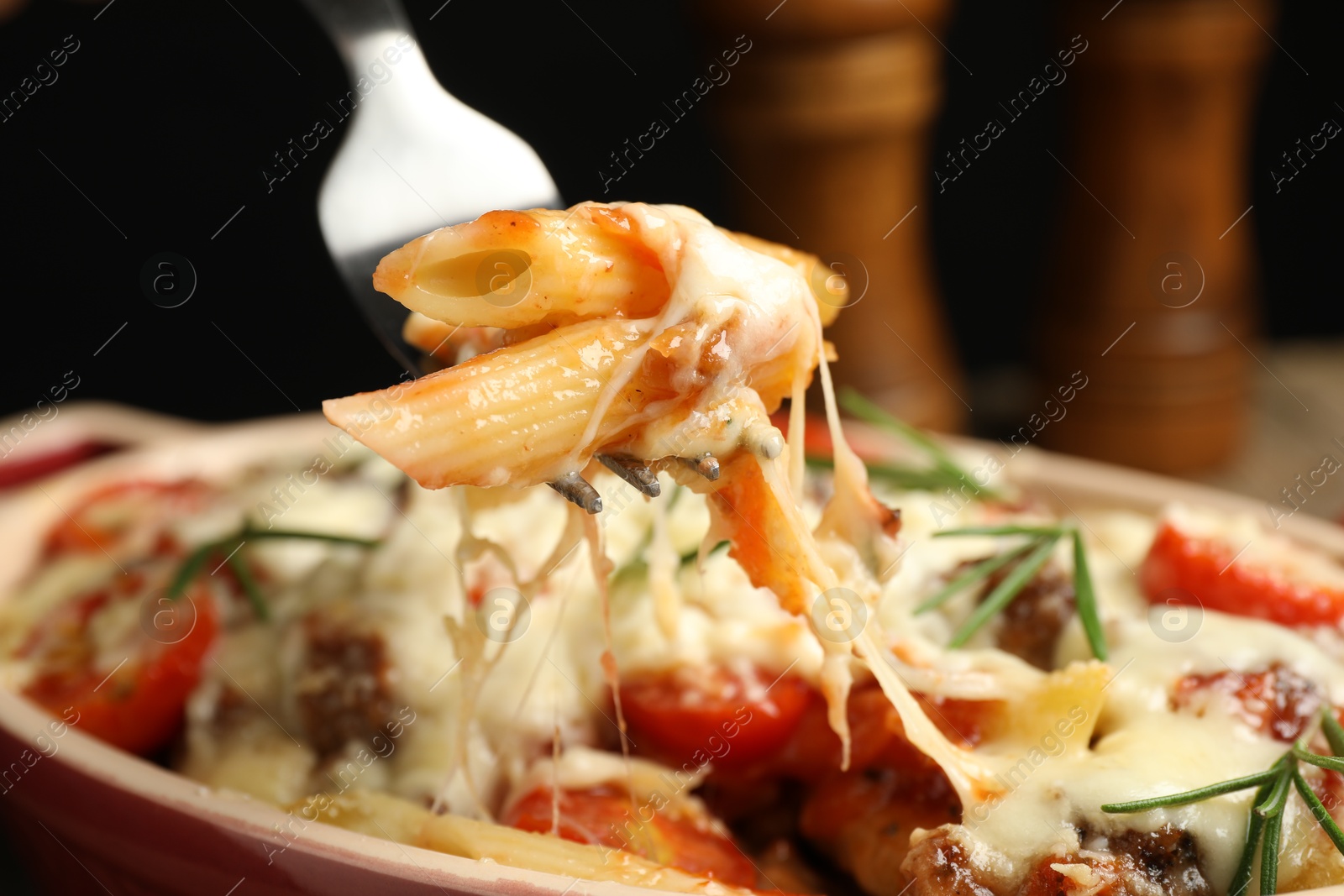 Photo of Eating delicious pasta casserole with fork against blurred black background, closeup