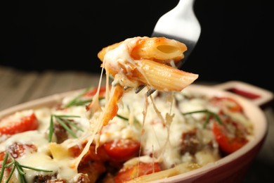 Photo of Eating delicious pasta casserole with fork against blurred black background, closeup