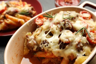 Photo of Delicious pasta casserole with cheese, tomatoes, minced meat and rosemary in baking dish on table, closeup