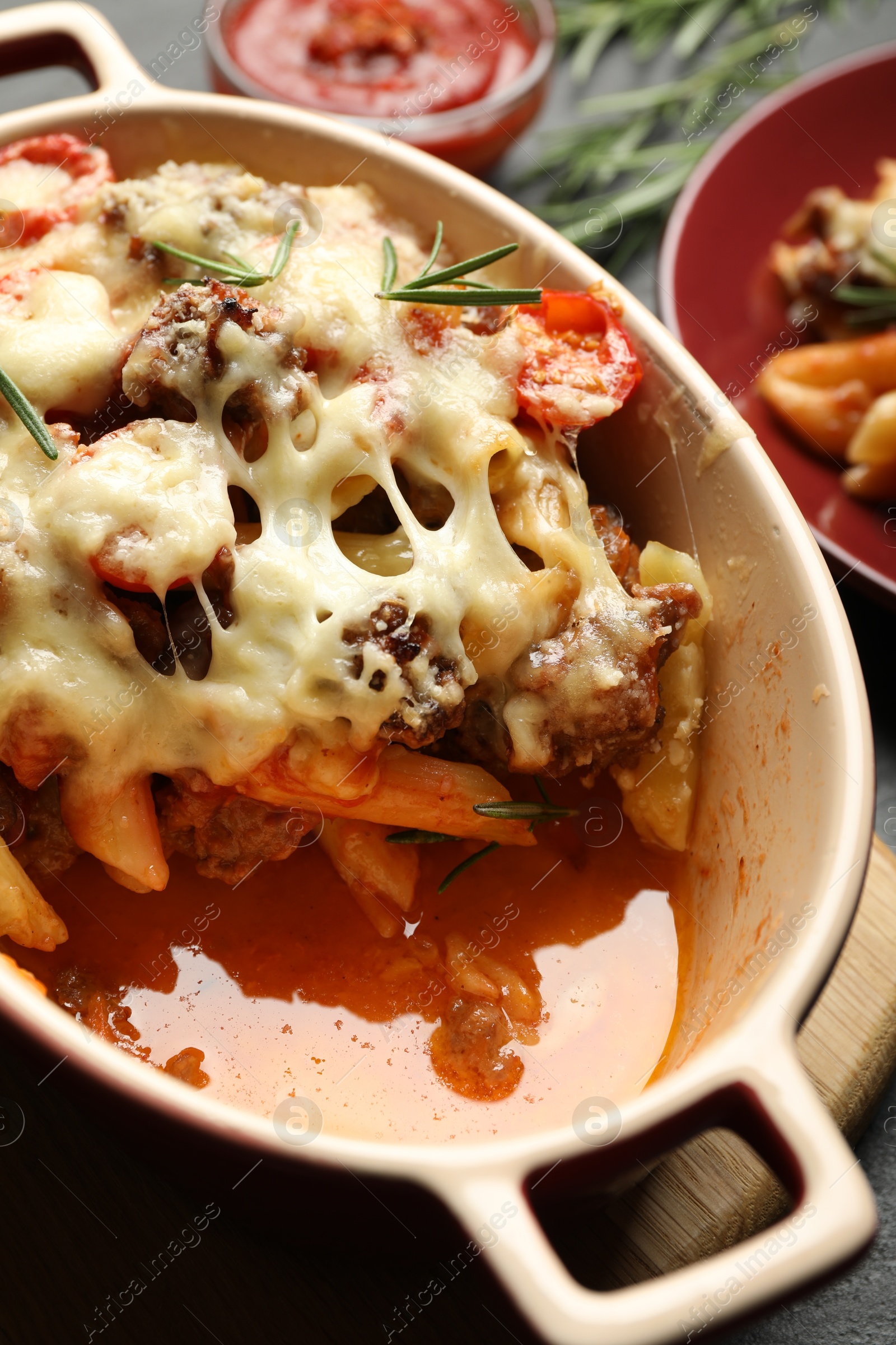 Photo of Delicious pasta casserole with cheese, tomatoes, minced meat and rosemary in baking dish on table, closeup