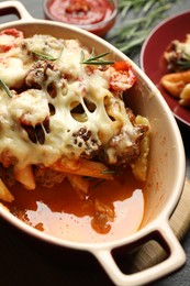 Photo of Delicious pasta casserole with cheese, tomatoes, minced meat and rosemary in baking dish on table, closeup