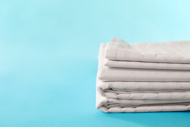 Photo of Stacked clean bed linens on light blue background, space for text