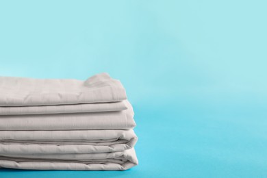 Photo of Stacked clean bed linens on light blue background, space for text