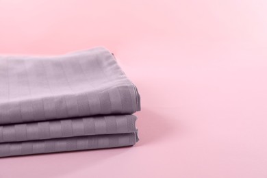 Photo of Stacked clean bed linens on pink background, closeup. Space for text