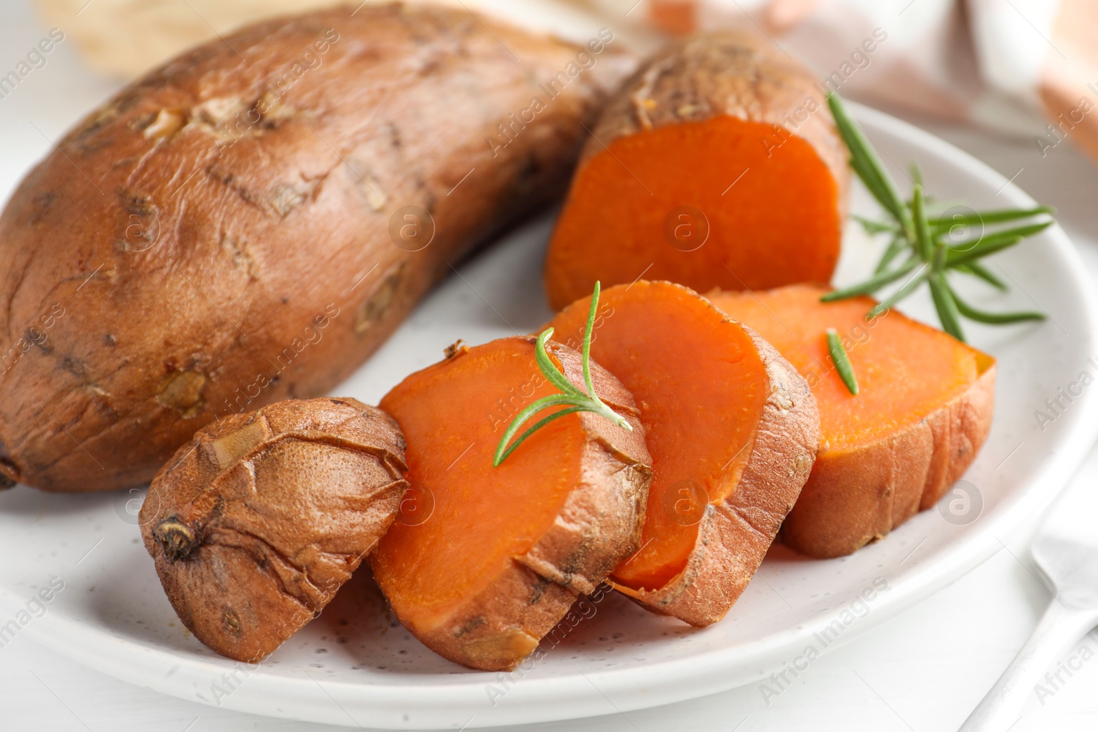 Photo of Tasty cooked sweet potatoes and rosemary on table, closeup