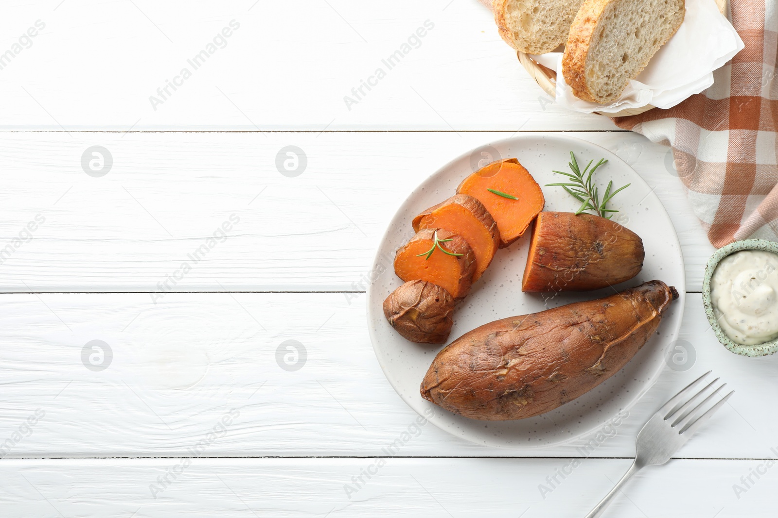 Photo of Tasty cooked sweet potatoes served with rosemary and sauce on white wooden table, top view. Space for text