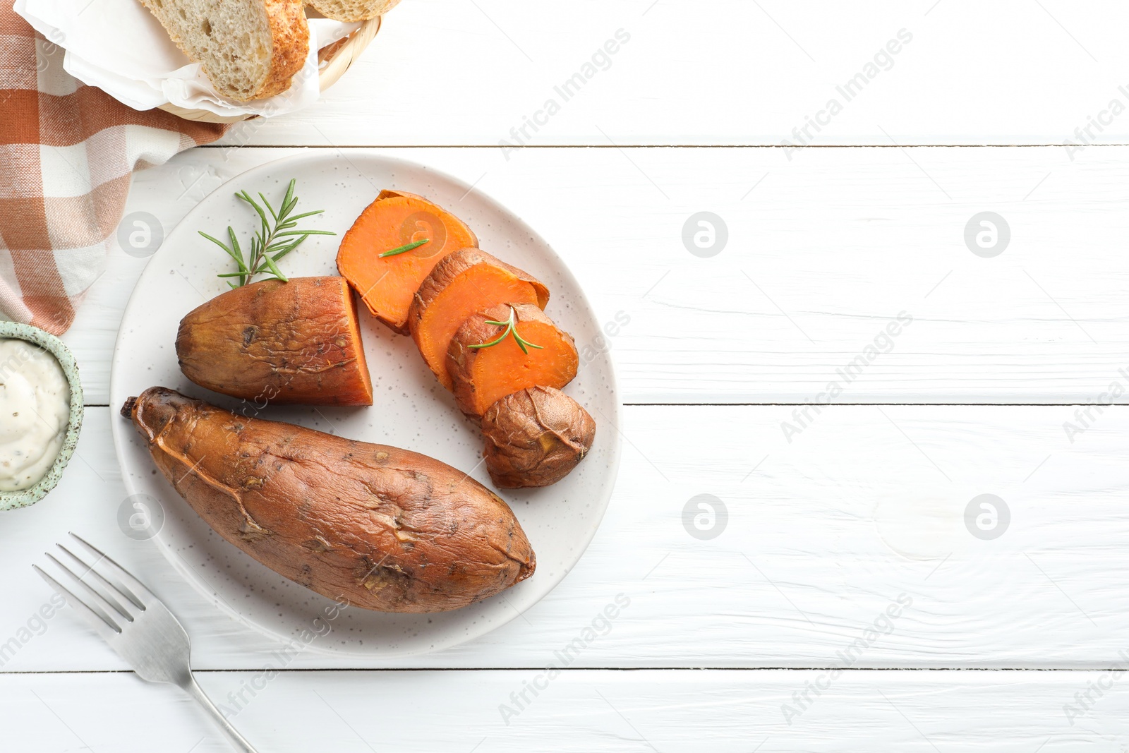 Photo of Tasty cooked sweet potatoes served with rosemary and sauce on white wooden table, top view. Space for text